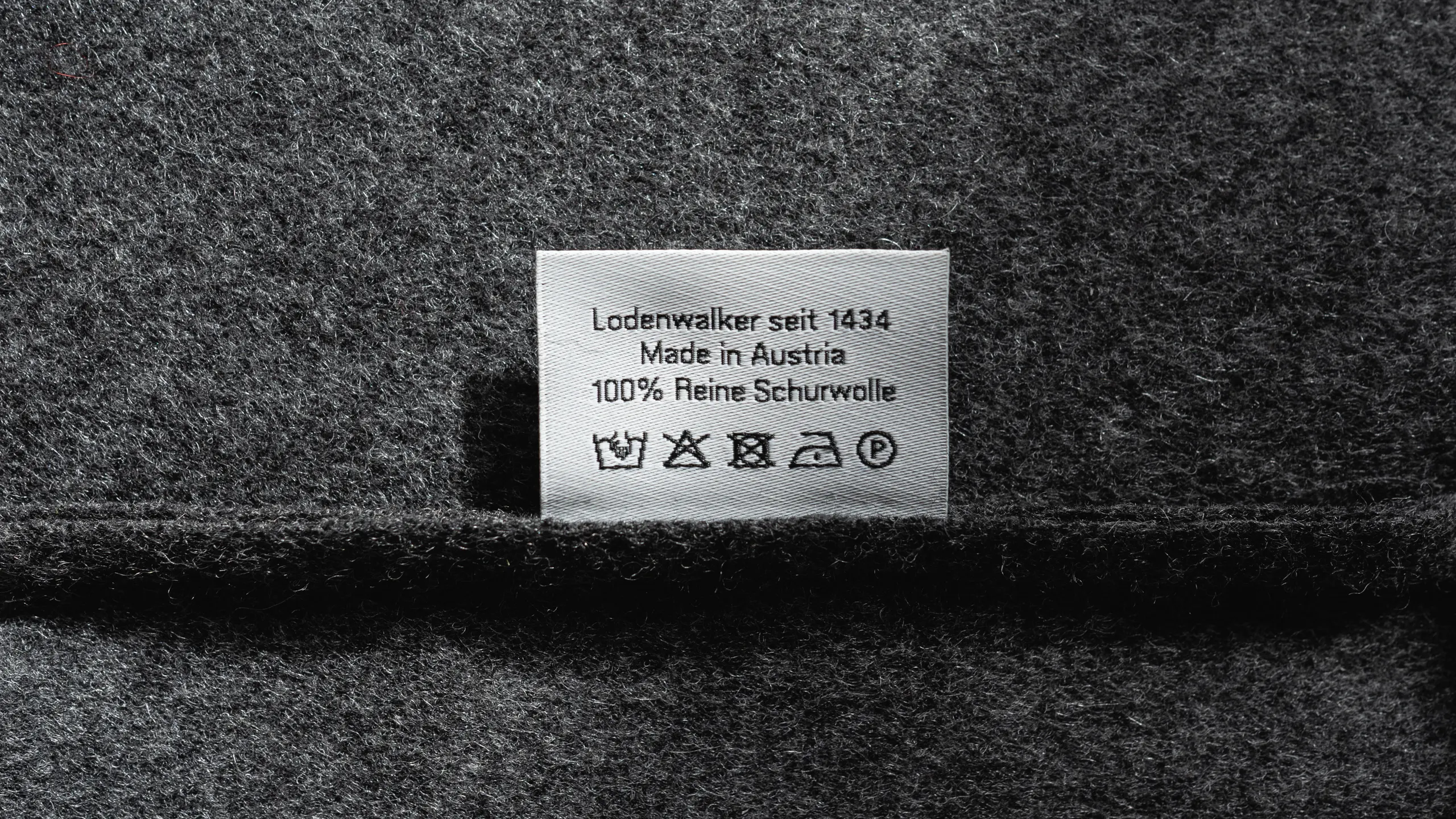 Pflegeetikett mit Waschanleitung für Schurwolle auf grauem Kleidungsstück aus Tuchloden